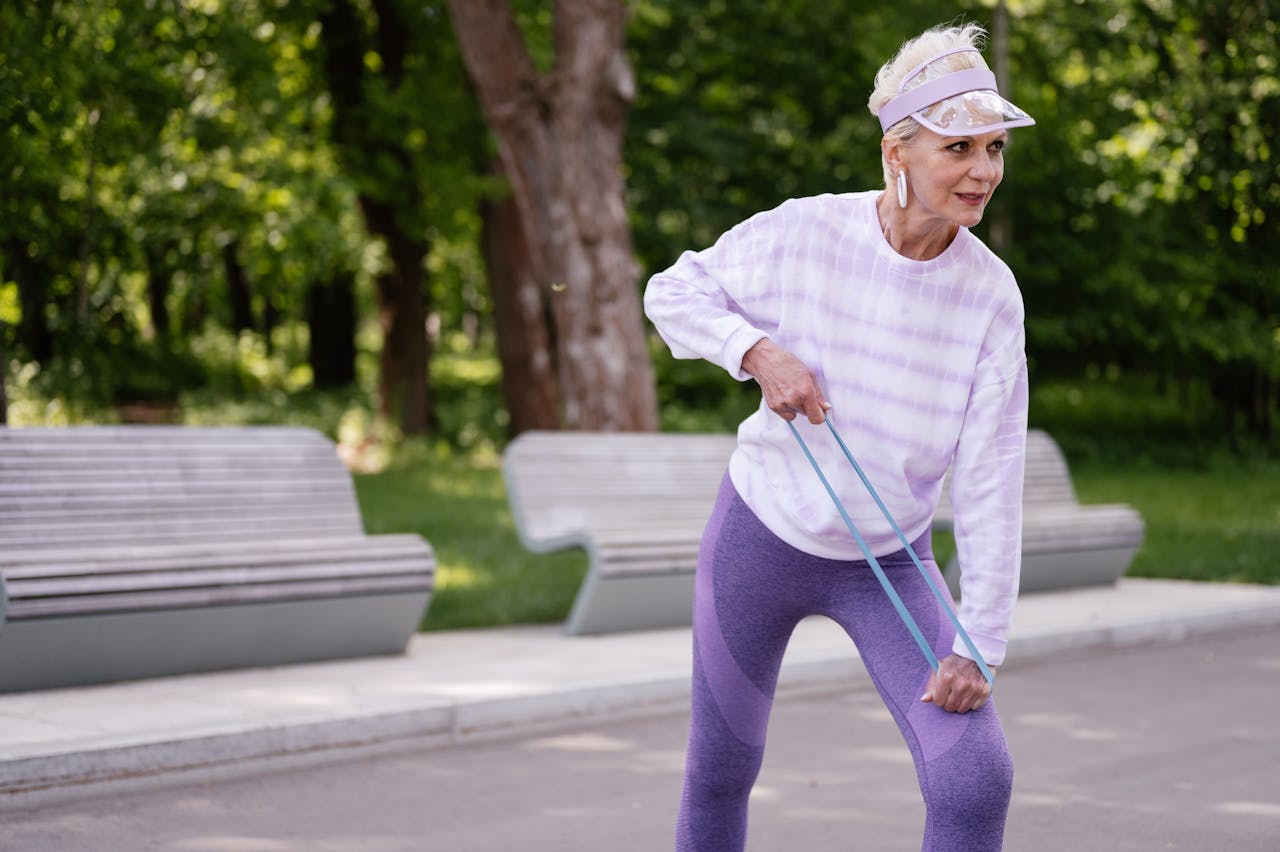 gallery-01 Senior woman performing outdoor exercise with a resistance band in a park setting.